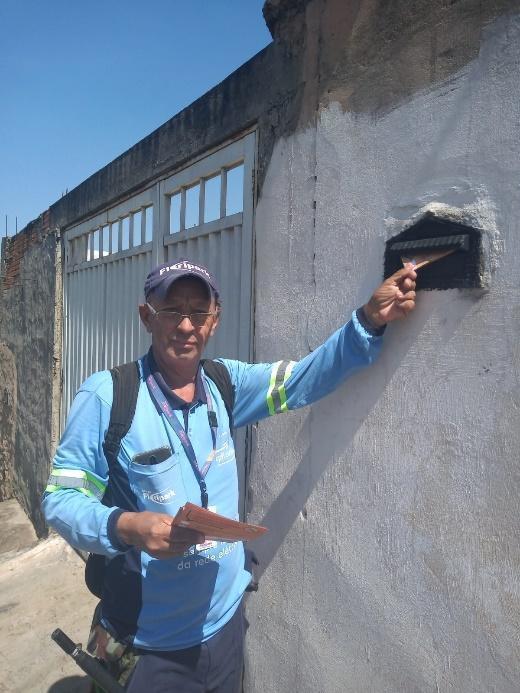 Foto de um homem vestindo uma blusa azul da CPFL colocando uma conta de energia em uma caixa de correio